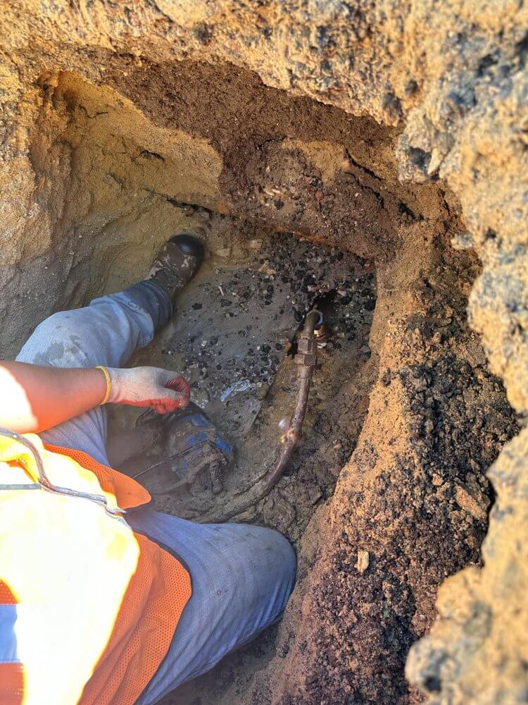 Construction worker repairing underground water pipe in trench.
