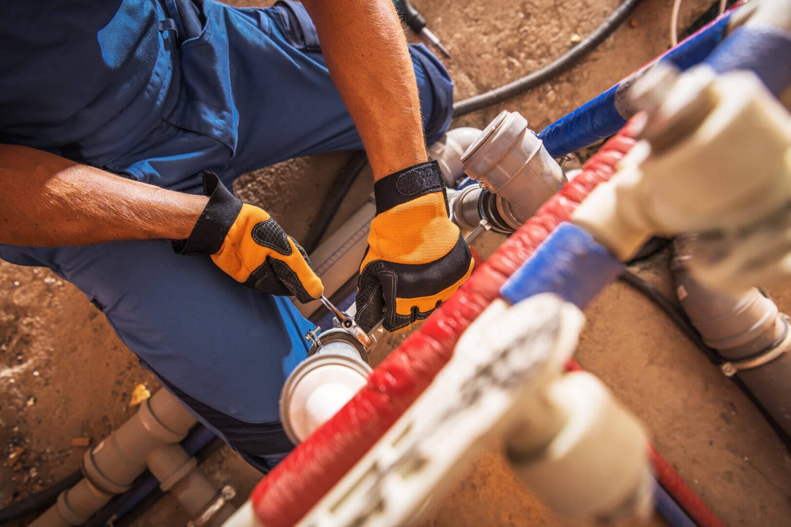 Professional plumber using tools to repair pipes in a construction area, wearing gloves and work attire.