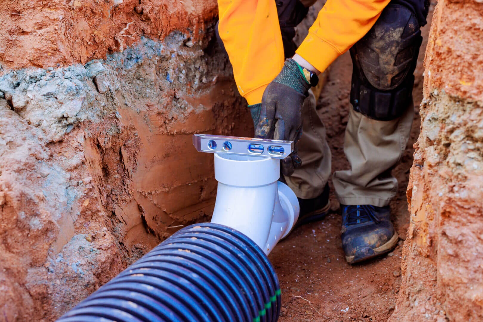 Worker uses precision tools to install drainage system at construction site during workday.