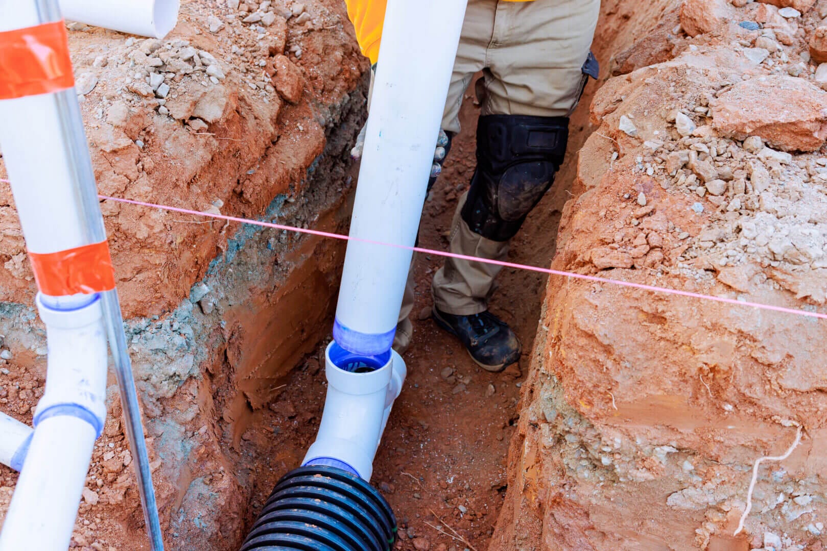 Workers installing drainage pipes in trench at construction site, daylight, soil excavation, plumbing infrastructure.